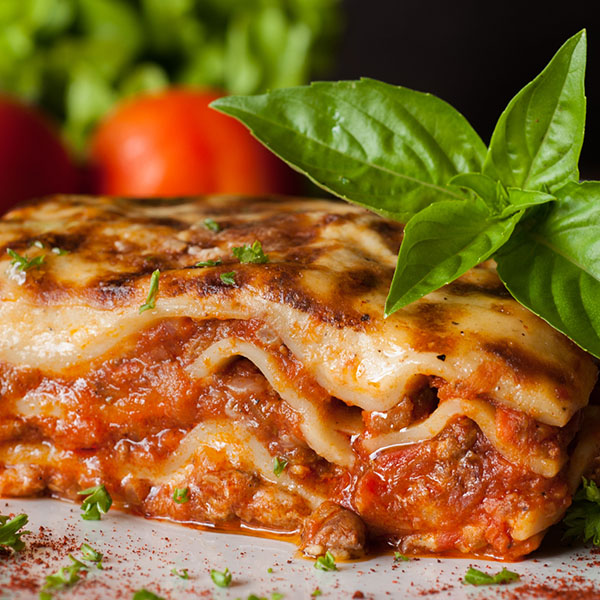 Lasagna on a square white plate with Italian basil